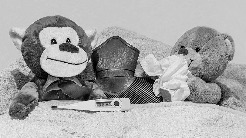 una scimmietta e un orsacchiotto peluche sono a letto malati con termometro, fazzoletto e borsa dell'acqua calda 